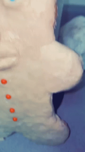 A Close Up Of A Gingerbread Man Covered In Frosting And Orange Buttons GIF