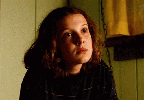 A Close Up Of A Girl 'S Face With A Yellow Curtain Behind Her GIF