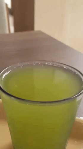 A Close Up Of A Glass Of Green Liquid On A Table . GIF
