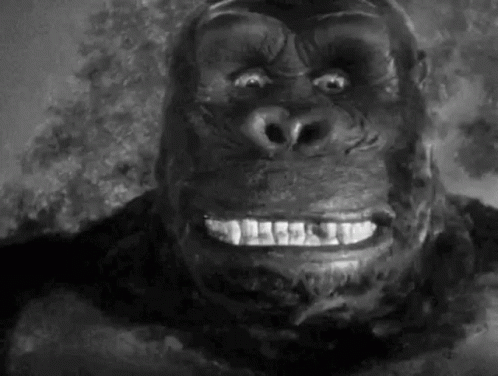 a close up of a gorilla 's face with a smile on it 's face in a black and white photo .