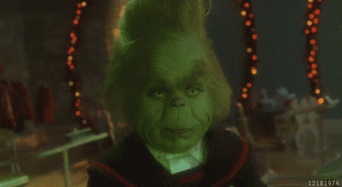 A Close Up Of A Grinch 'S Face In A Dark Room With Christmas Lights In The Background . GIF