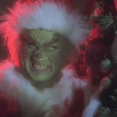 A Close Up Of A Grinch 'S Face With A Wreath In The Background . GIF