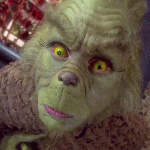 A Close Up Of A Grinch 'S Face With Bright Yellow Eyes GIF