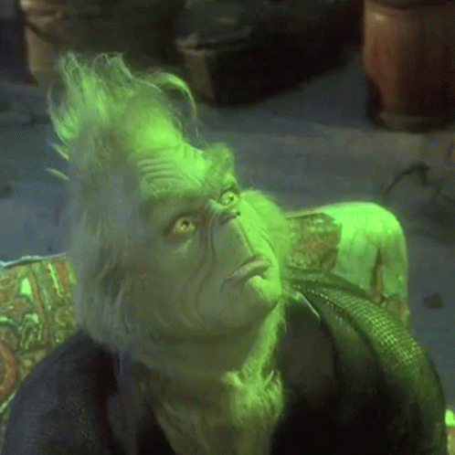A Close Up Of A Grinch Sitting On A Couch With His Eyes Closed . GIF