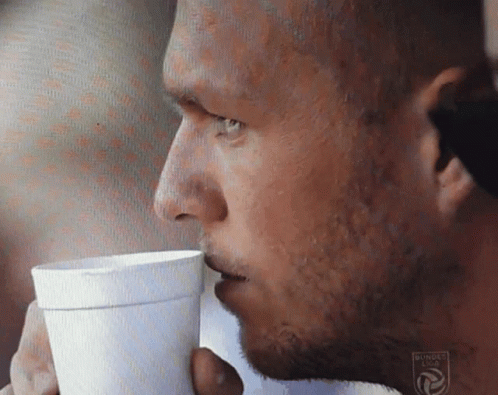 A Close Up Of A Man Drinking From A Cup That Says Bundesliga On It GIF