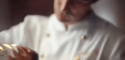 A Close Up Of A Man In A Chef 'S Uniform Holding A Piece Of Food . GIF