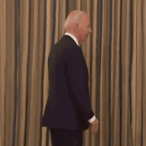 A Close Up Of A Man In A Suit And Tie Smiling In Front Of A Curtain . GIF