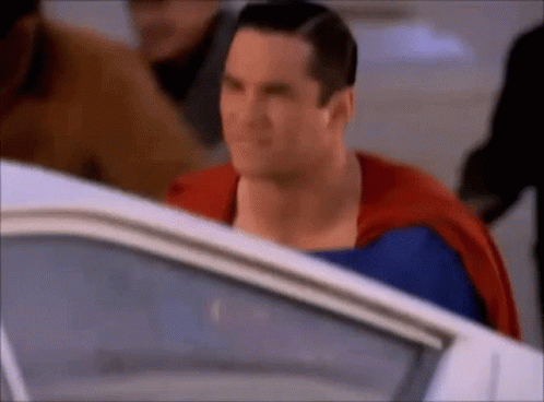 A Close Up Of A Man In A Superman Costume Standing Next To A White Car . GIF