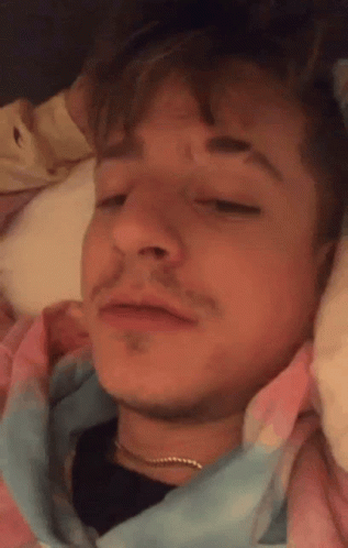 A Close Up Of A Man Laying In Bed With His Eyes Closed And A Tie Dye Shirt On . GIF