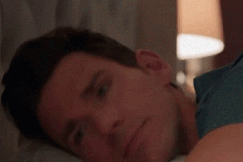 A Close Up Of A Man Laying On A Bed With His Head On His Arm . GIF