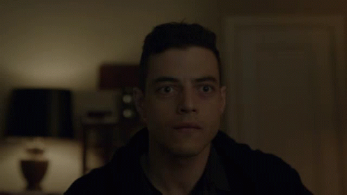 A Close Up Of A Man 'S Face In A Dark Room With A Lamp In The Background GIF