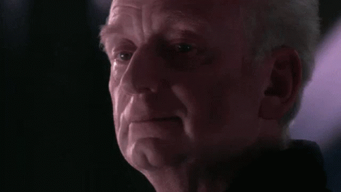 A Close Up Of A Man 'S Face In A Dark Room With A Purple Light Behind Him . GIF