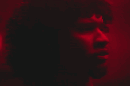A Close Up Of A Man 'S Face In A Dark Room With A Red Light Behind Him GIF