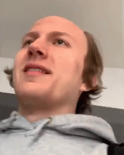 A Close Up Of A Man 'S Face With A Bald Head And A Gray Hoodie . GIF