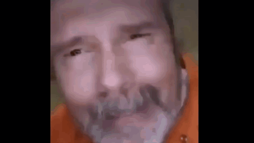 A Close Up Of A Man 'S Face With A Beard And A Orange Shirt . GIF