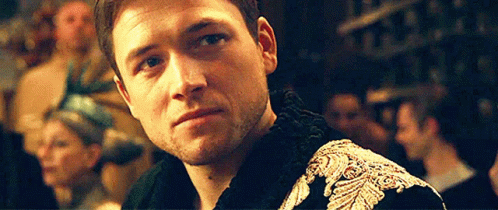 A Close Up Of A Man 'S Face With A Beard Wearing A Black And Gold Jacket . GIF
