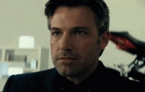 A Close Up Of A Man 'S Face With A Beard Wearing A Black Suit And Tie . GIF