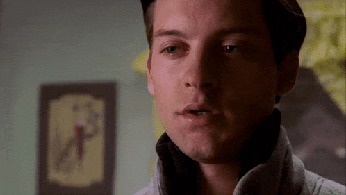 A Close Up Of A Man 'S Face With A Clock On The Wall Behind Him GIF