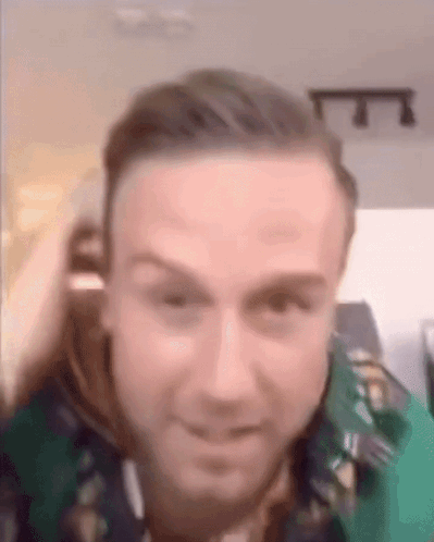 A Close Up Of A Man 'S Face With A Green Shirt On And A Blurred Background . GIF