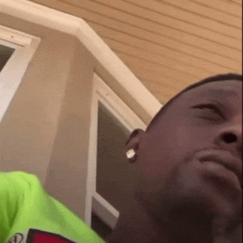 A Close Up Of A Man 'S Face With A Green Shirt On And Earrings . GIF