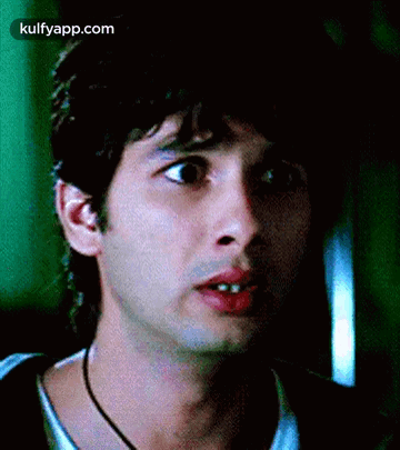 A Close Up Of A Man 'S Face With A Necklace Around His Neck And A Green Background . GIF