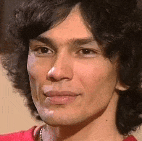 A Close Up Of A Man 'S Face With A Red Shirt On And A Necklace Around His Neck . GIF