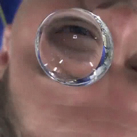 A Close Up Of A Man 'S Face With A Reflection Of Him In A Glass Ball GIF