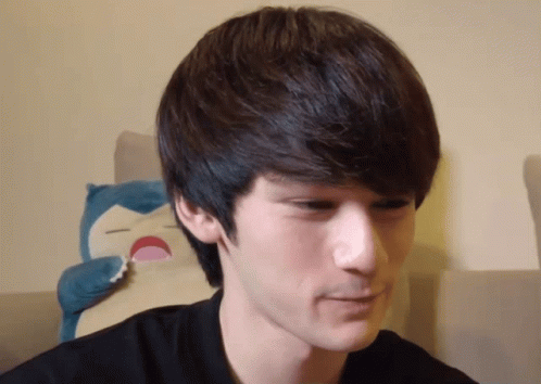 A Close Up Of A Man 'S Face With A Stuffed Animal Behind Him GIF
