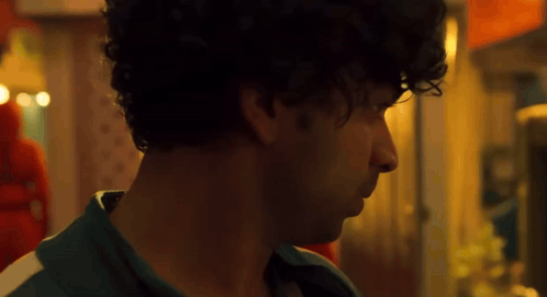 A Close Up Of A Man 'S Face With Curly Hair Looking At Something . GIF