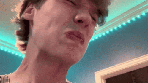 A Close Up Of A Man 'S Face With His Eyes Closed And A Blue Wall In The Background . GIF
