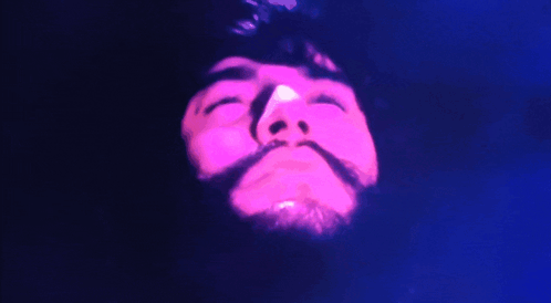 A Close Up Of A Man 'S Face With His Eyes Closed And A Pink Light Behind Him GIF