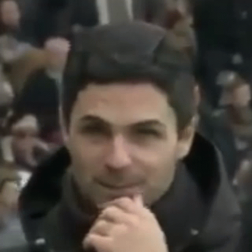 A Close Up Of A Man 'S Face With His Hands Folded And A Crowd Behind Him . GIF