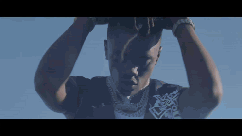 A Close Up Of A Man 'S Face With His Hands On His Head Against A Blue Sky GIF