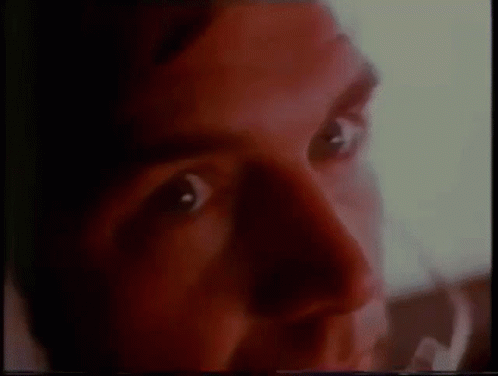 A Close Up Of A Man 'S Face With Red Eyes And A Blurred Background . GIF