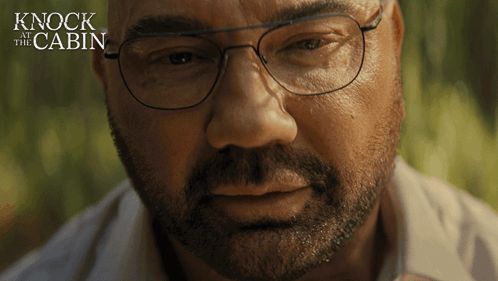 A Close Up Of A Man 'S Face With The Words " Knock At The Cabin " Behind Him GIF