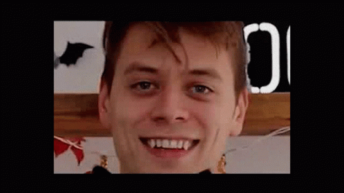 A Close Up Of A Man 'S Face With Vampire Teeth And A Bat In The Background . GIF