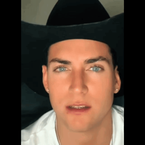 a close up of a man wearing a black cowboy hat and a white shirt .