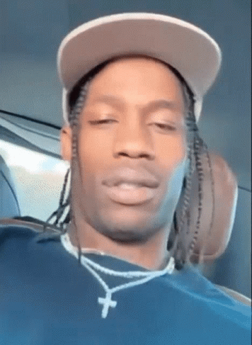 A Close Up Of A Man Wearing A Hat And A Necklace With A Cross On It . GIF