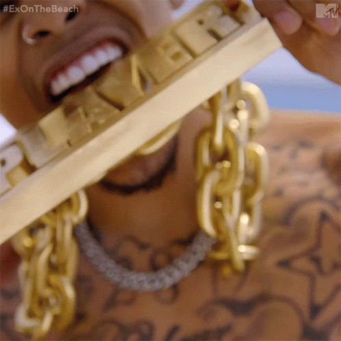 A Close Up Of A Man Wearing Gold Chains And A Gold Bar That Says Exon The Beach GIF