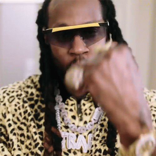 A Close Up Of A Man Wearing Sunglasses And A Necklace With The Word Trav On It GIF