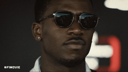 A Close Up Of A Man Wearing Sunglasses With #Fimovie Written Below Him GIF
