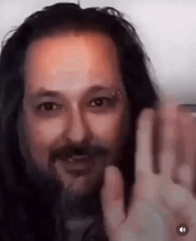 A Close Up Of A Man With Long Hair And A Beard Waving At The Camera . GIF