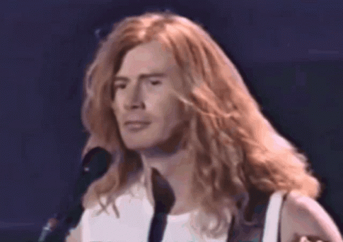 A Close Up Of A Man With Long Hair Singing Into A Microphone GIF