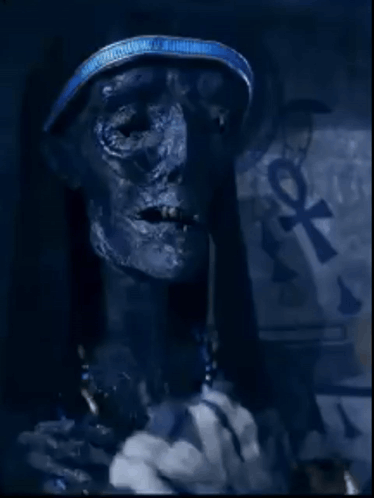 A Close Up Of A Mummy With An Ankh Symbol On The Wall Behind Him GIF