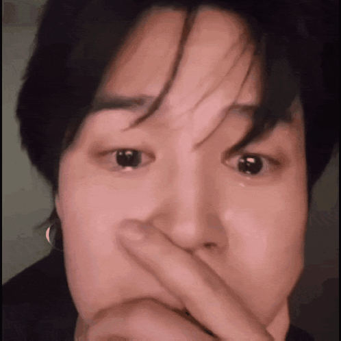 A Close Up Of A Person Covering Their Mouth With Their Finger . GIF