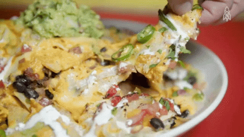 A Close Up Of A Person Eating Nachos With Guacamole On Top GIF