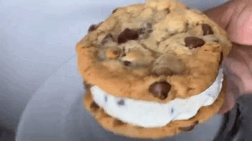 A Close Up Of A Person Holding A Chocolate Chip Cookie Sandwich With Ice Cream . GIF