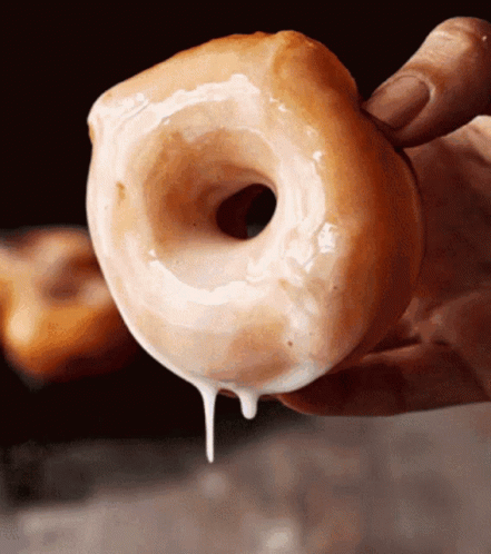 A Close Up Of A Person Holding A Glazed Doughnut GIF