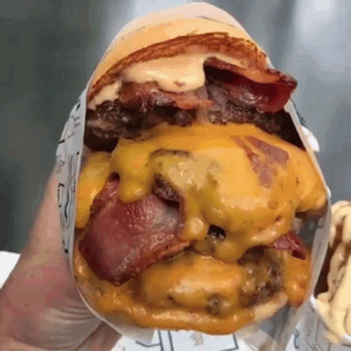 A Close Up Of A Person Holding A Hamburger With Cheese And Bacon On A Bun . GIF