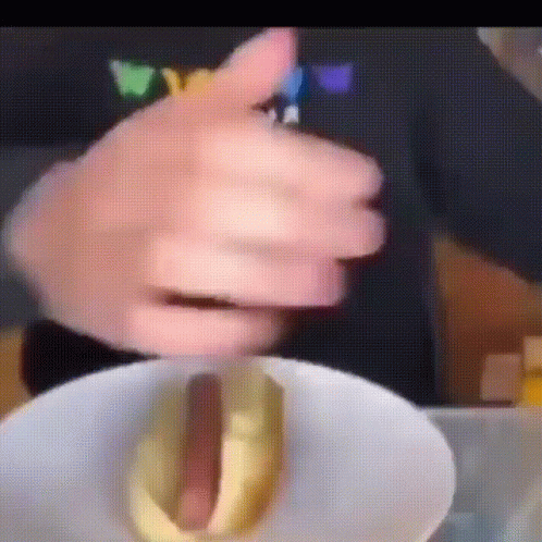 A Close Up Of A Person Holding A Hot Dog With Mustard On It GIF